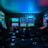 Dimly lit gaming arcade featuring a variety of brightly illuminated slot machines and video gaming screens. Neon signs and colorful displays create a vibrant atmosphere. The arrangement of gaming machines suggests an inviting space for entertainment, with chairs positioned for players.